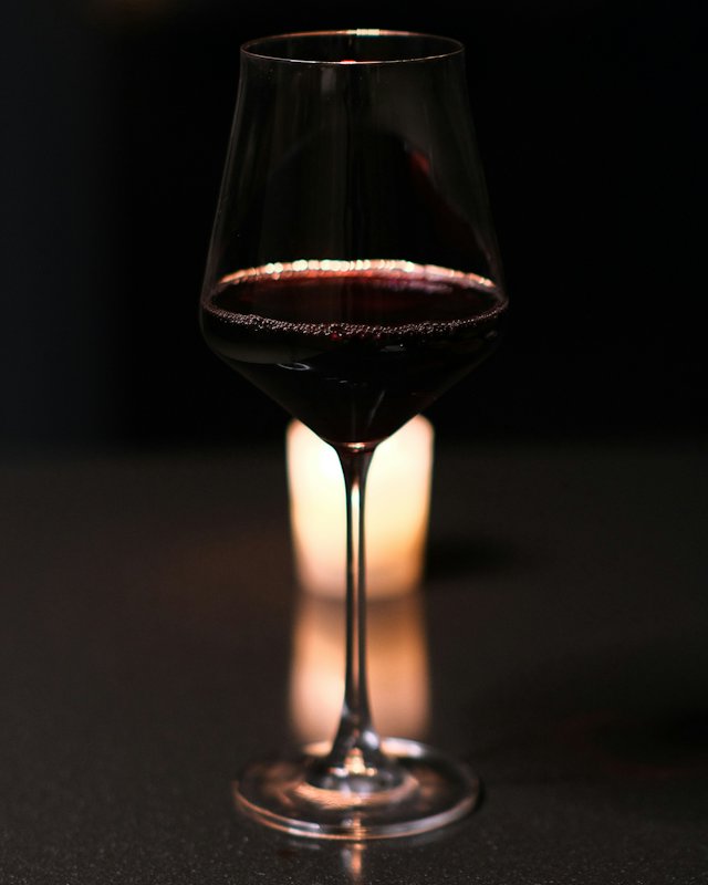 Glas Rotwein im Kerzenlicht vor dunklem Hintergrund